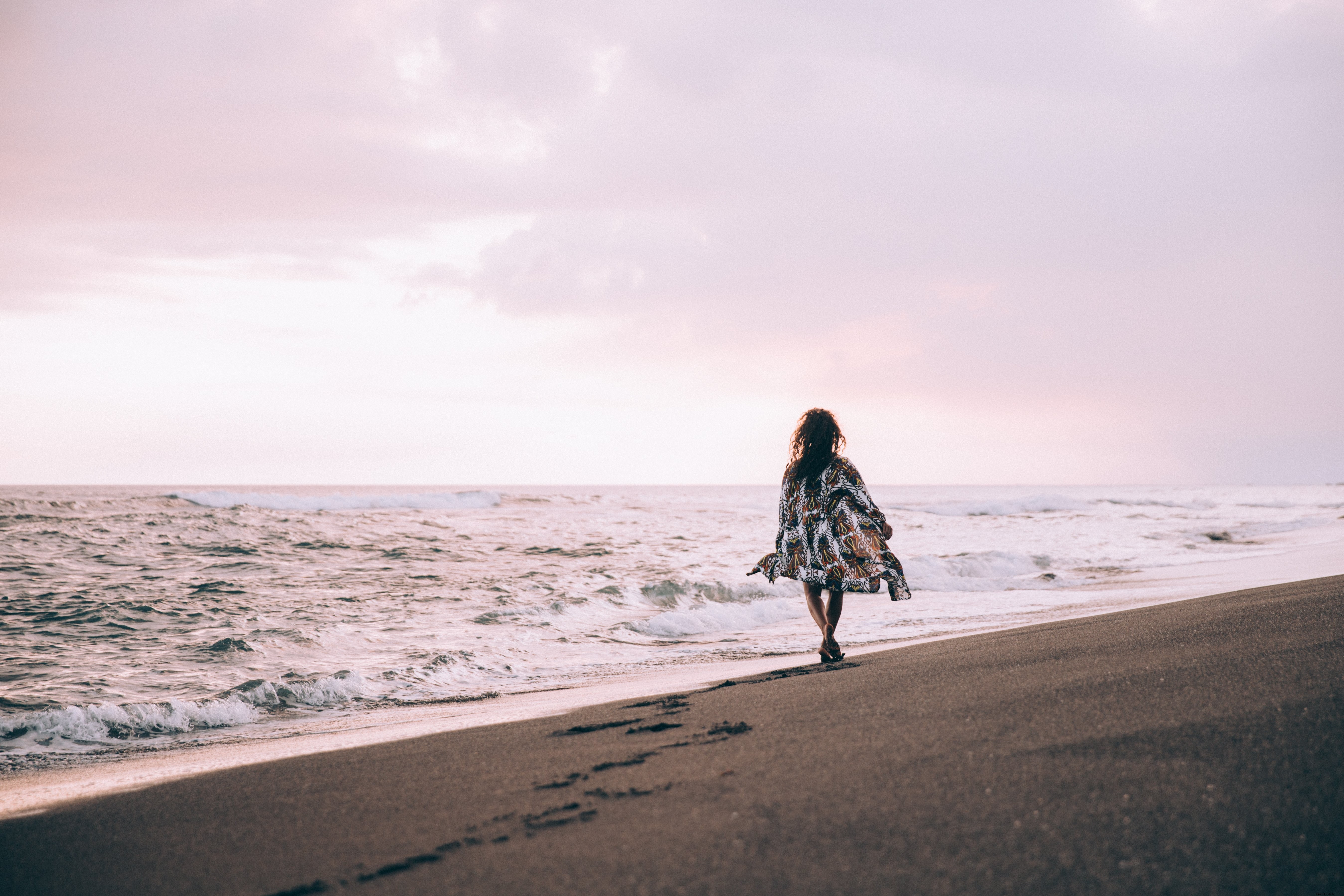 Femme bronzée en robe fluide, promenade le long de la plage