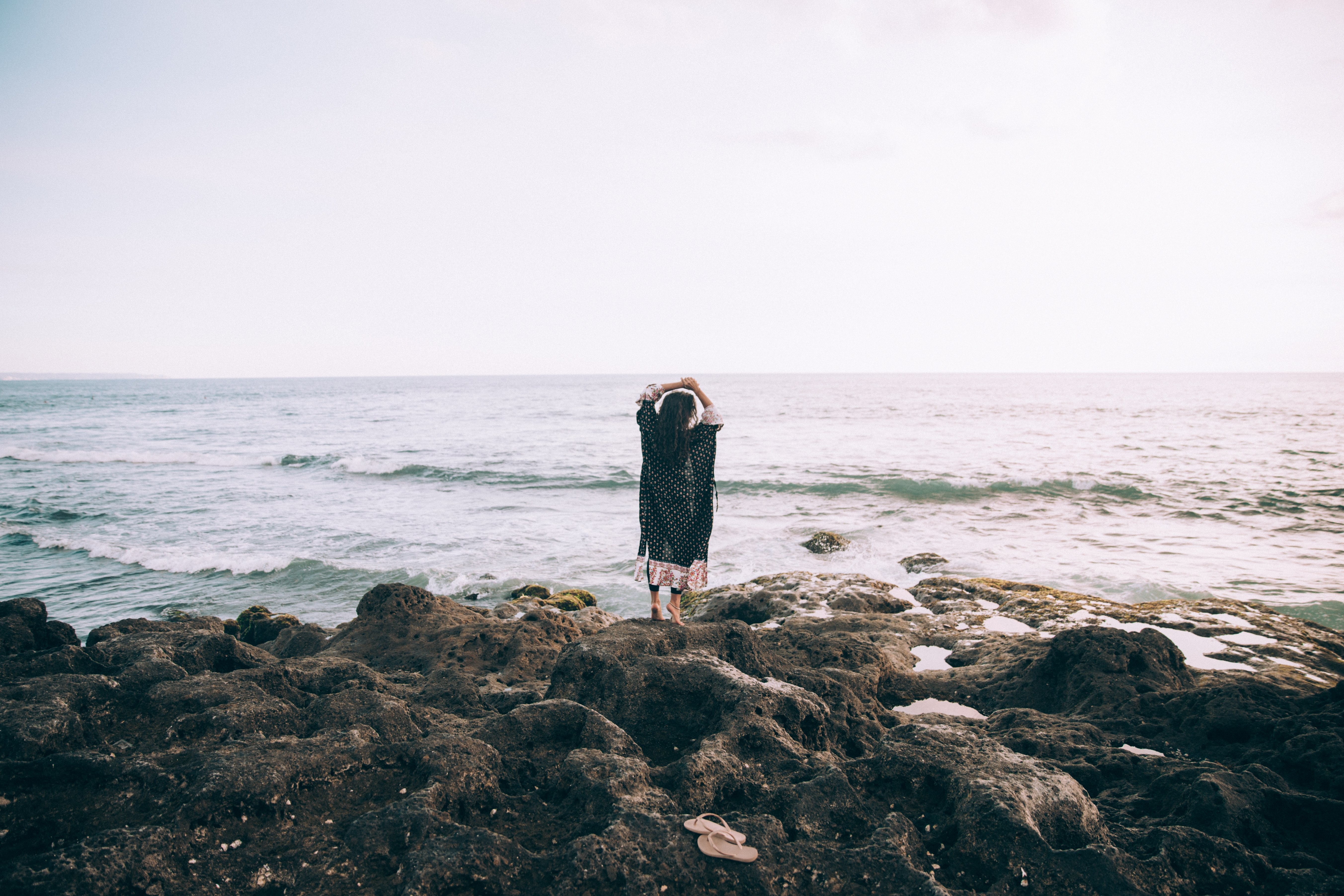 Une femme au bord de la mer, les mains levées, dans une photo féérique