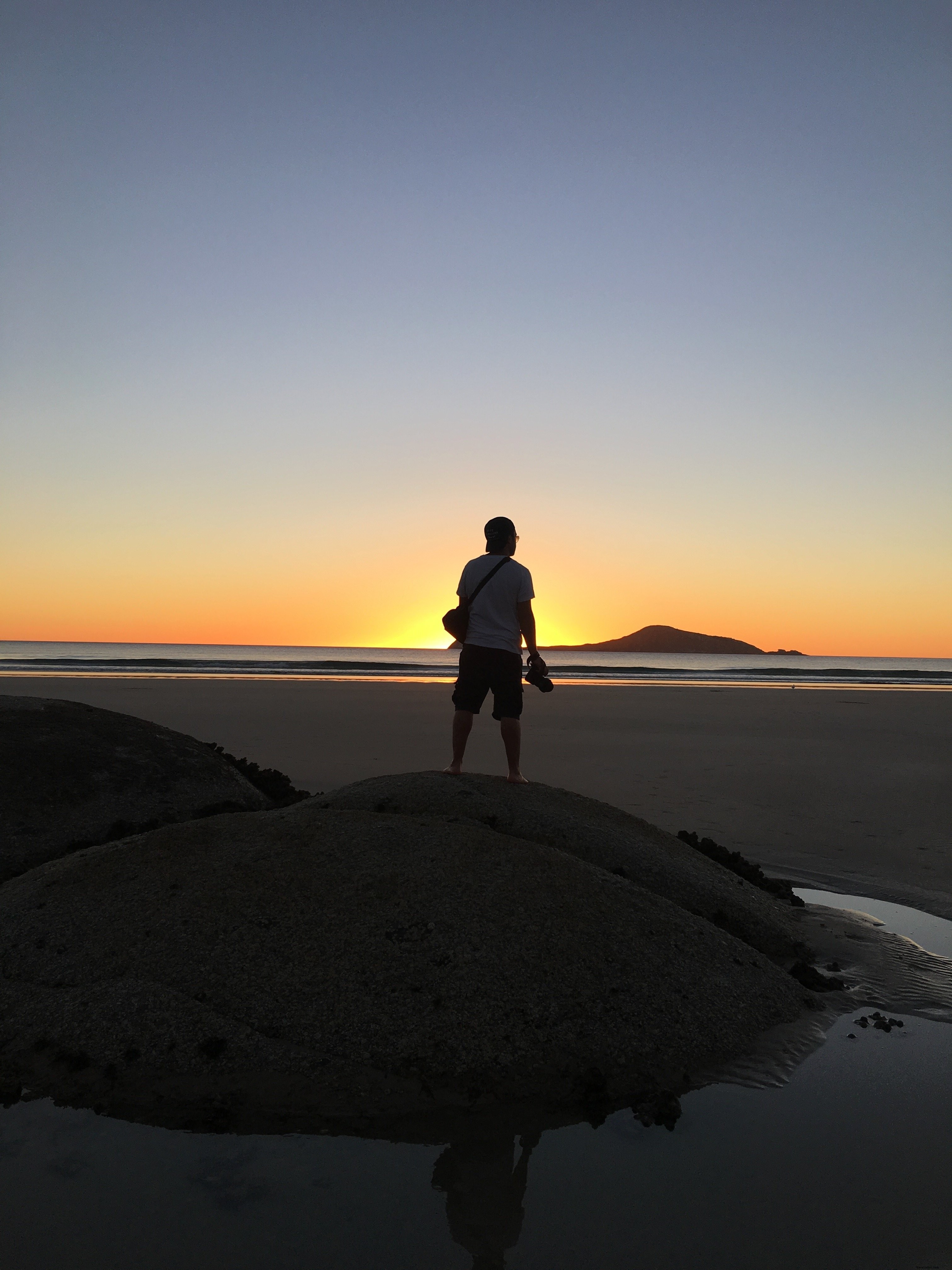 Un homme sur une dune admire le coucher du soleil depuis la plage