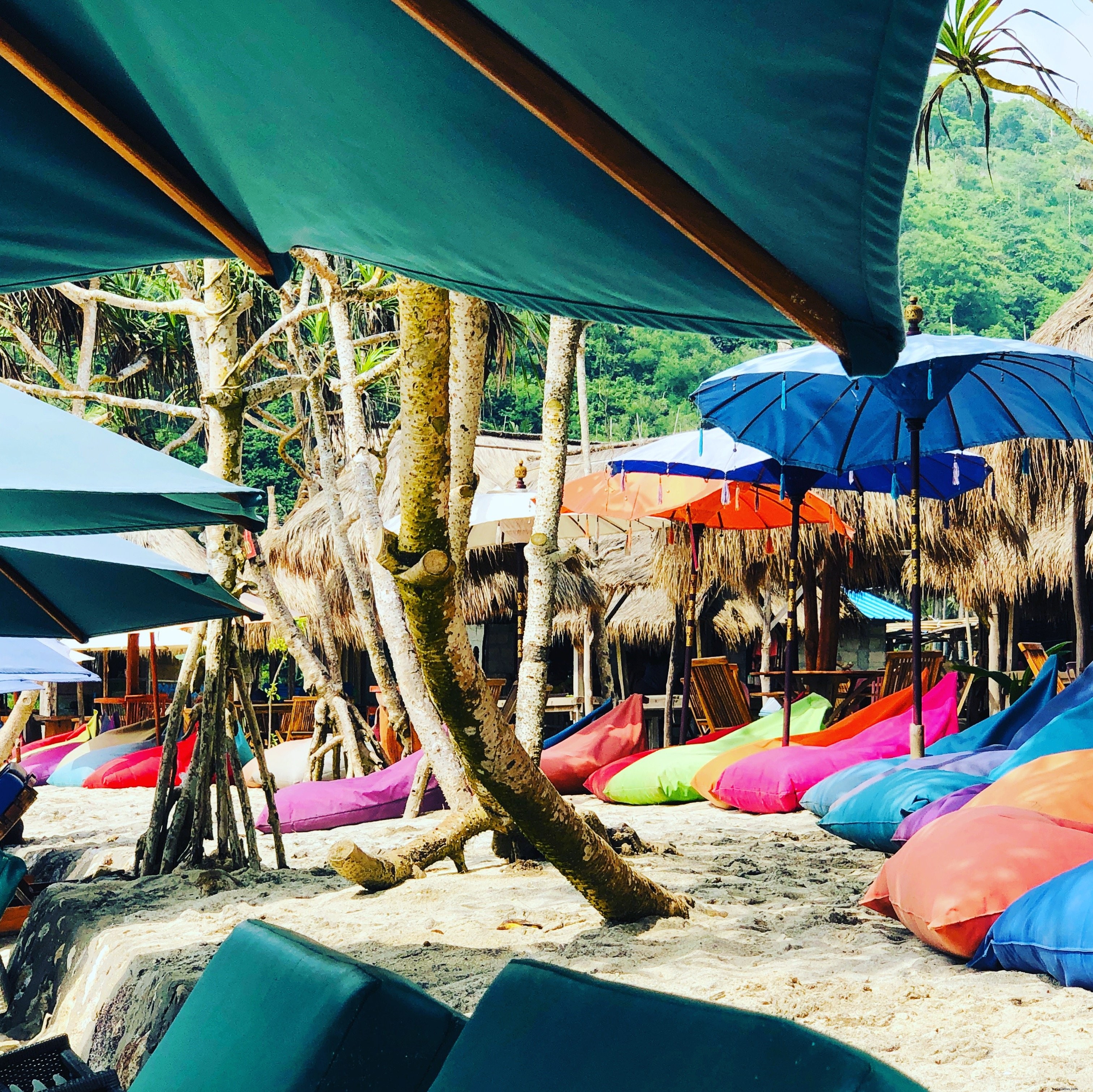 Poufs colorés sur une plage aux tons bleus, entourés d’arbres