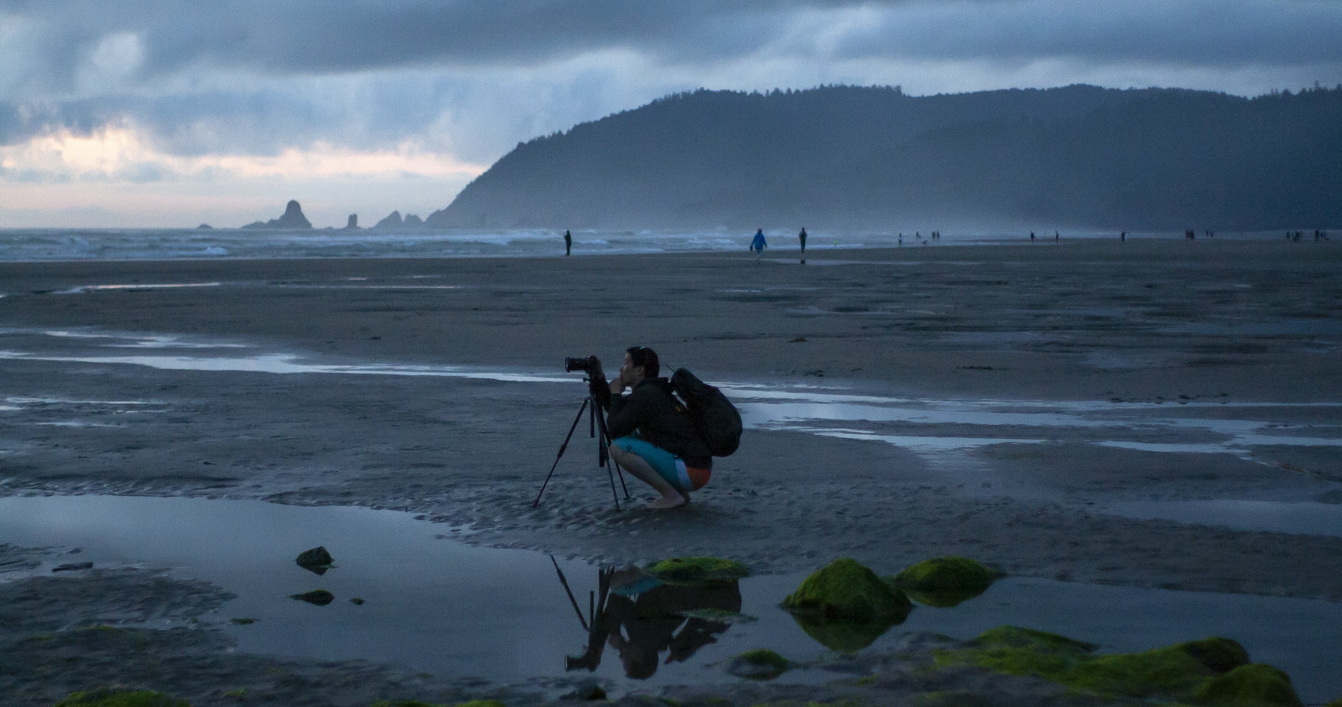 Photographe accroupi sur son trépied au bord d’une plage brumeuse