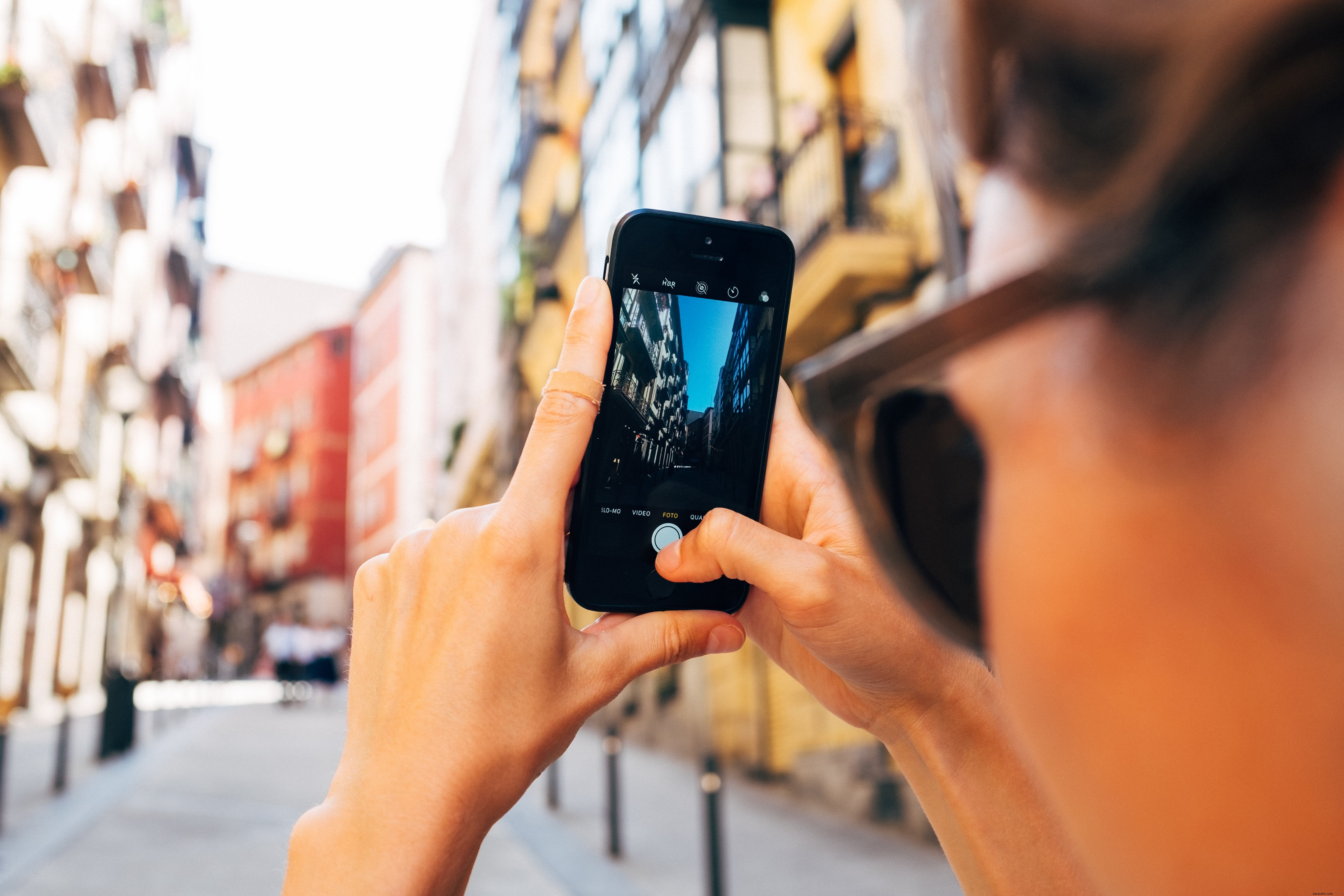 Une femme capture une scène de rue ensoleillée avec son smartphone
