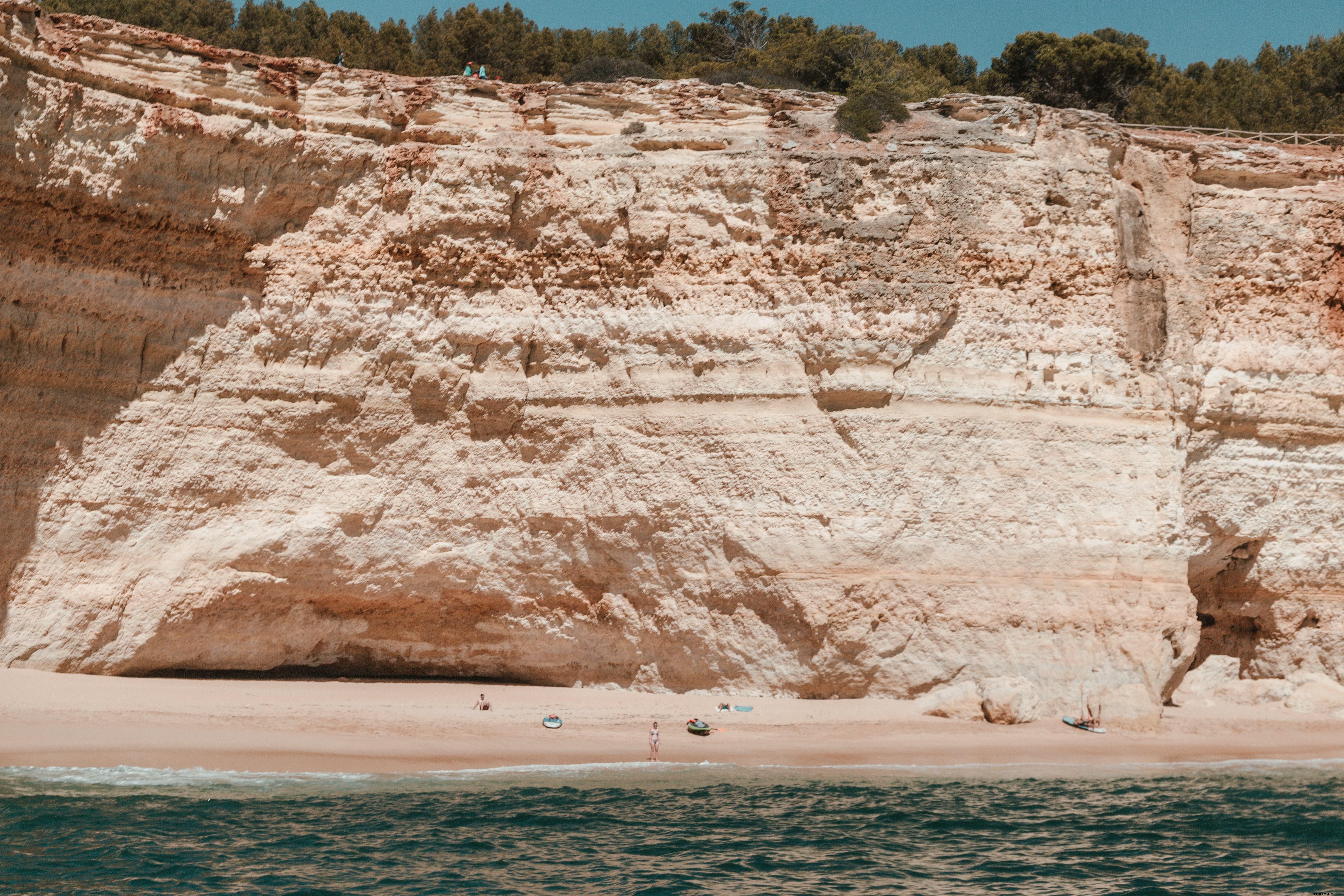 Kayakistes et surfeurs sur une plage de sable au pied de falaises calcaires