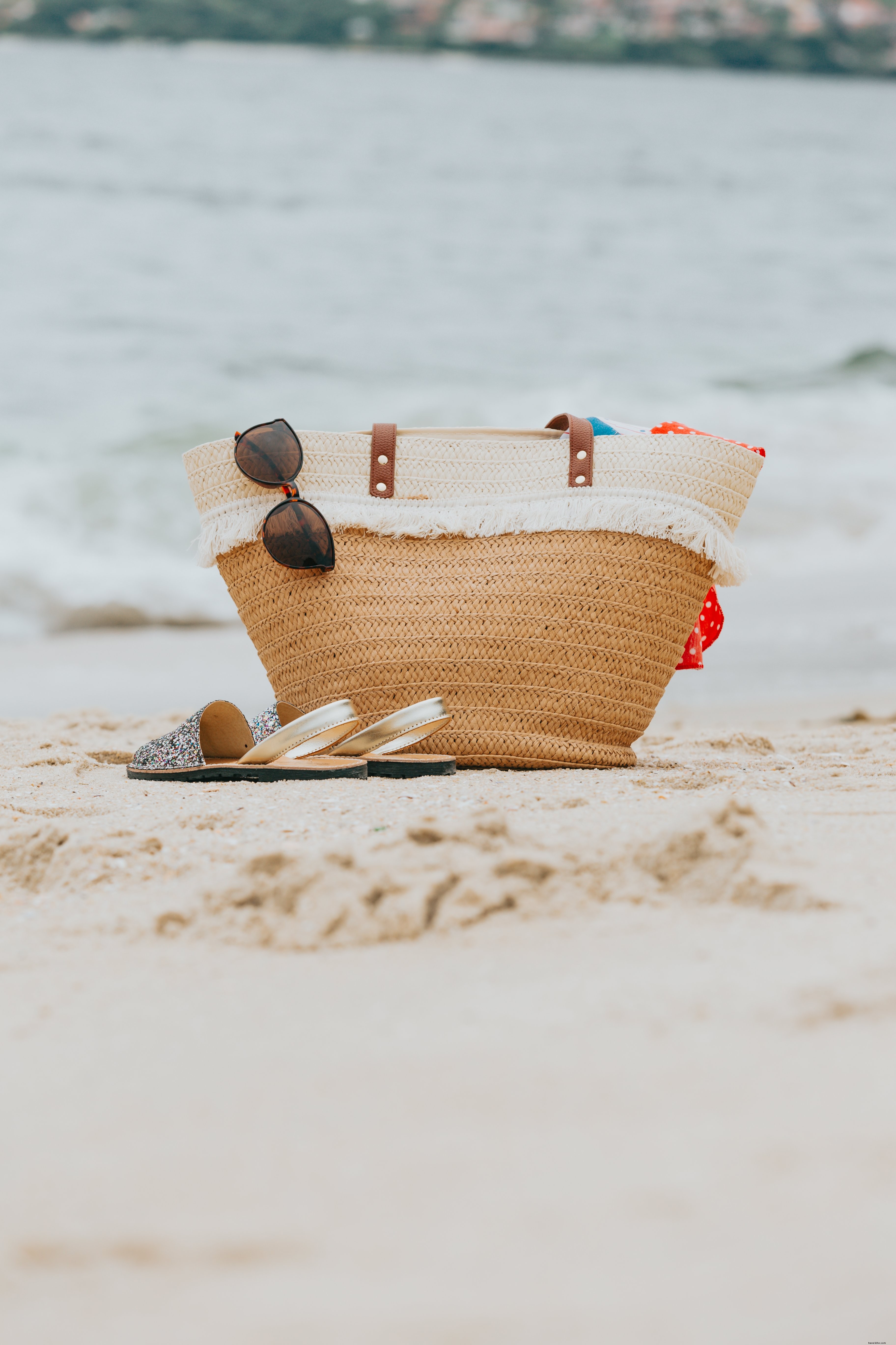 Sac de plage en osier et sandales sur une plage de sable blanc