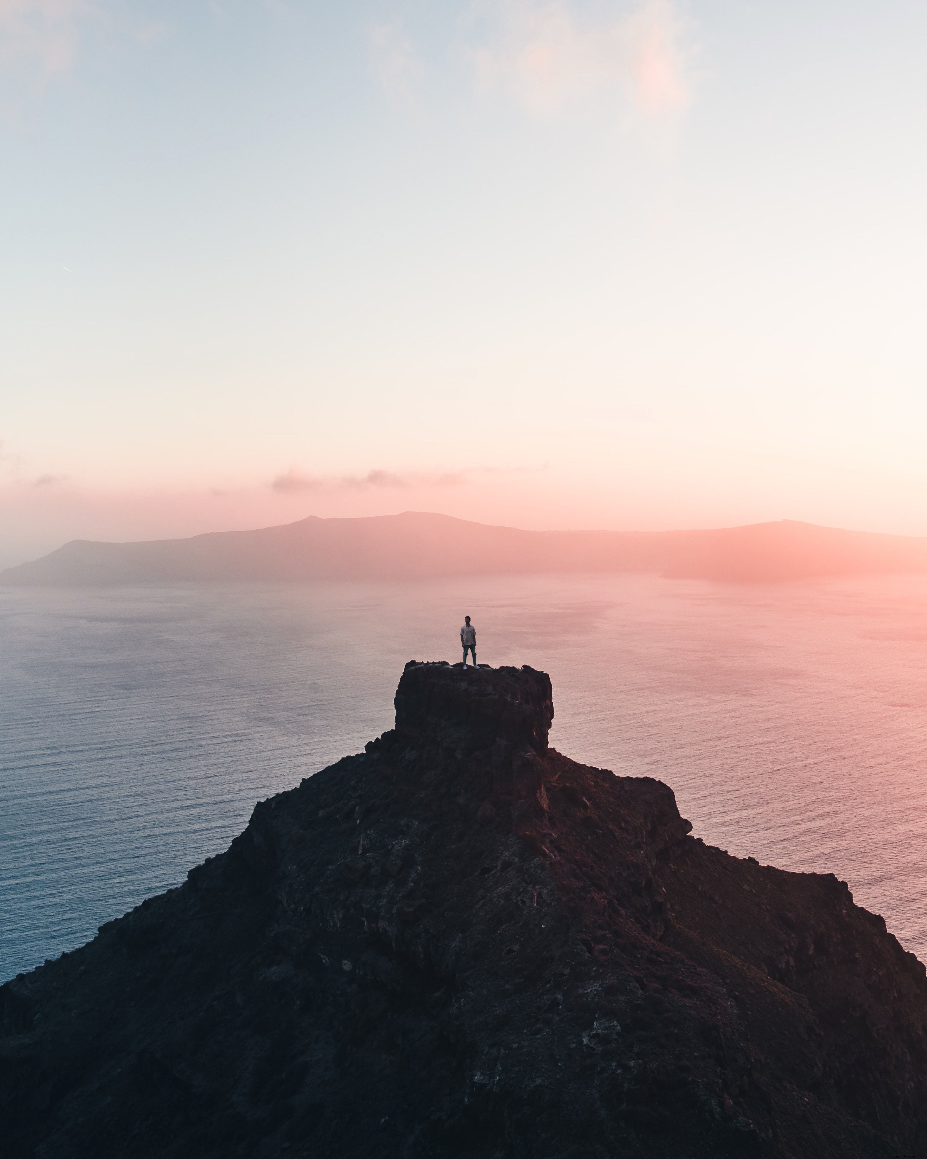 Une personne sur une falaise lointaine, capturant le coucher du soleil