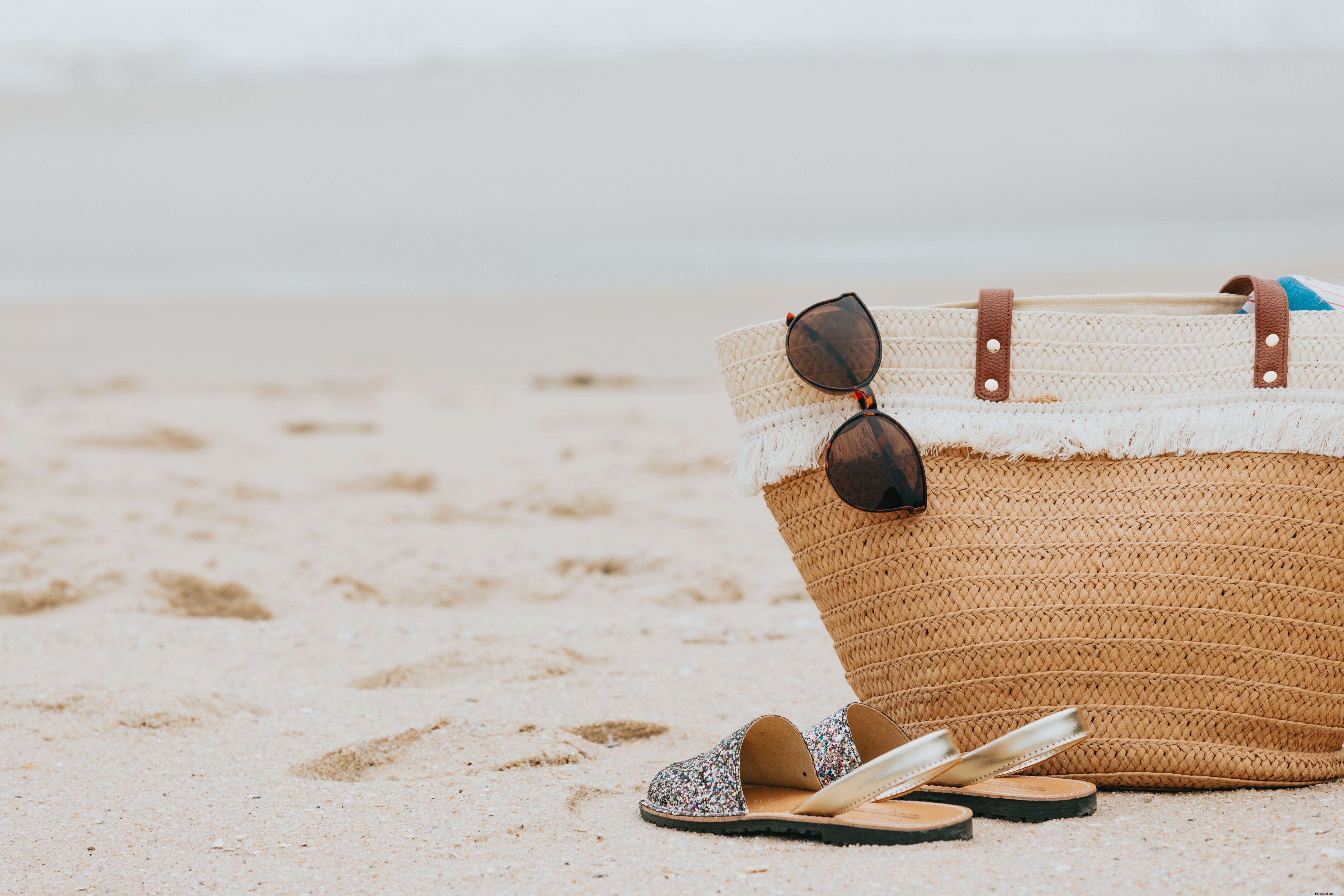 Photo d’une plage de sable avec lunettes de soleil, sandales et sac de plage