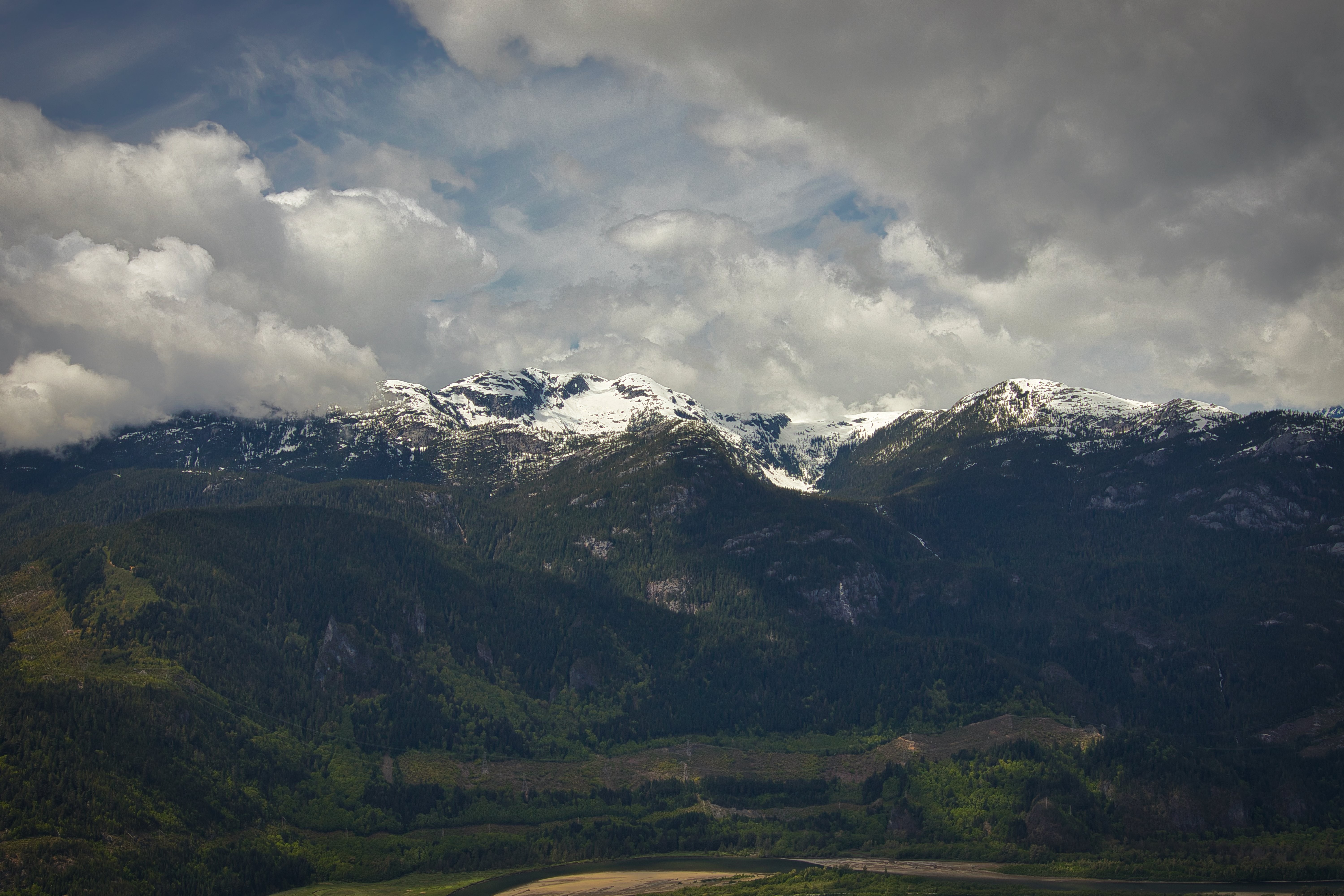 Photo : Montagnes verdoyantes enneigées sous des nuages duveteux