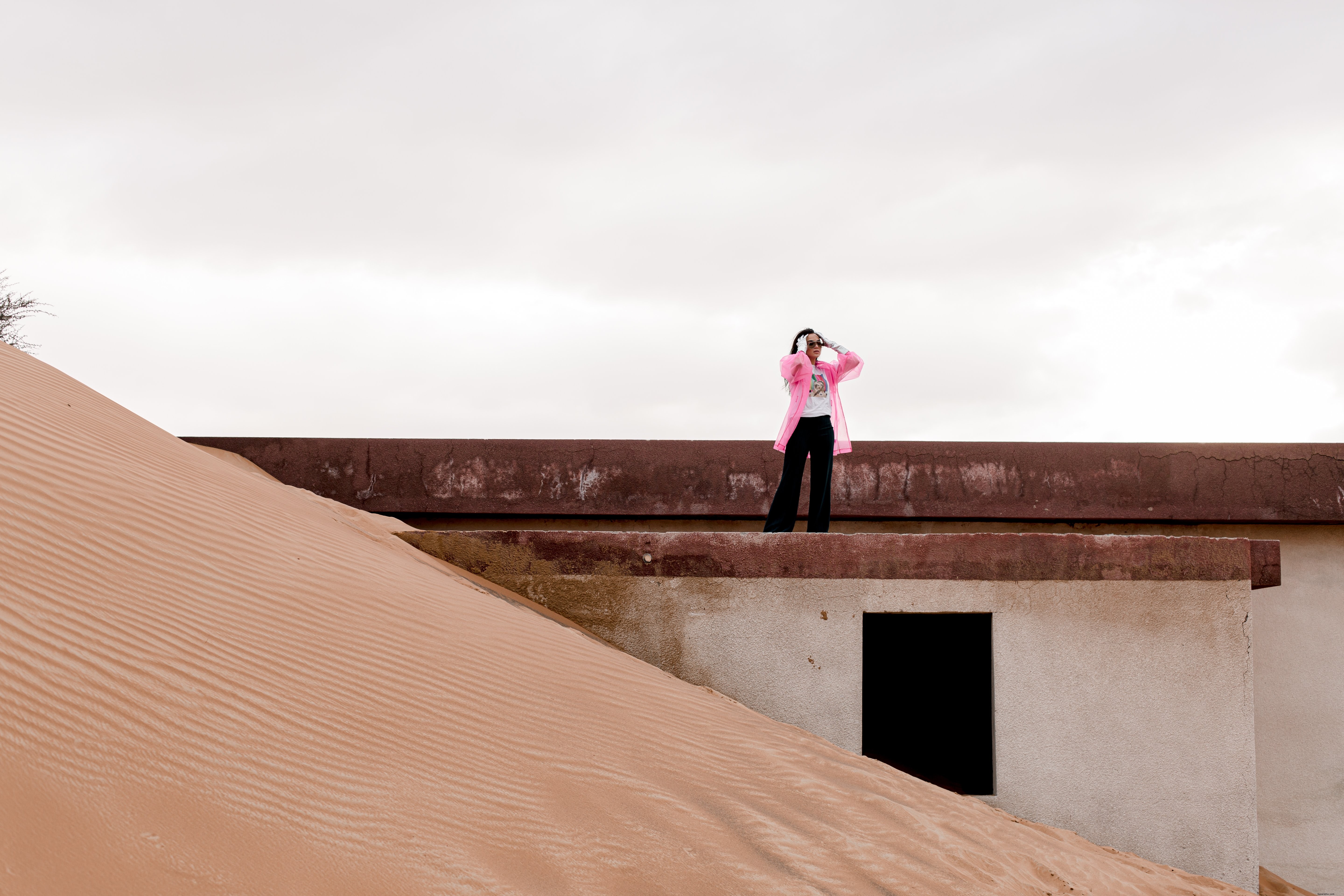 Une personne en veste rose se tient sur un bâtiment recouvert de sable – Photo