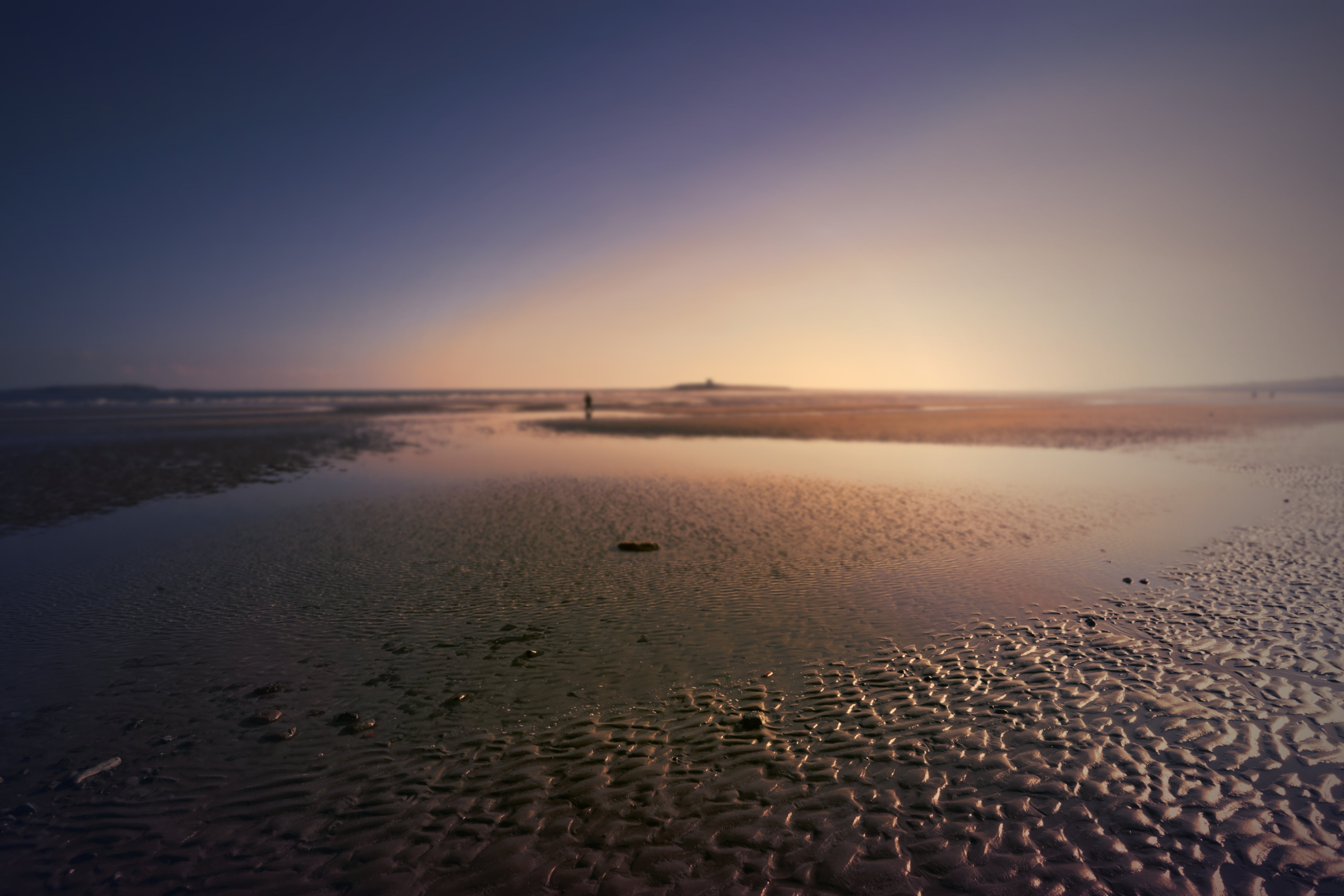 Photo d’une plage aux eaux peu profondes et d’une silhouette lointaine