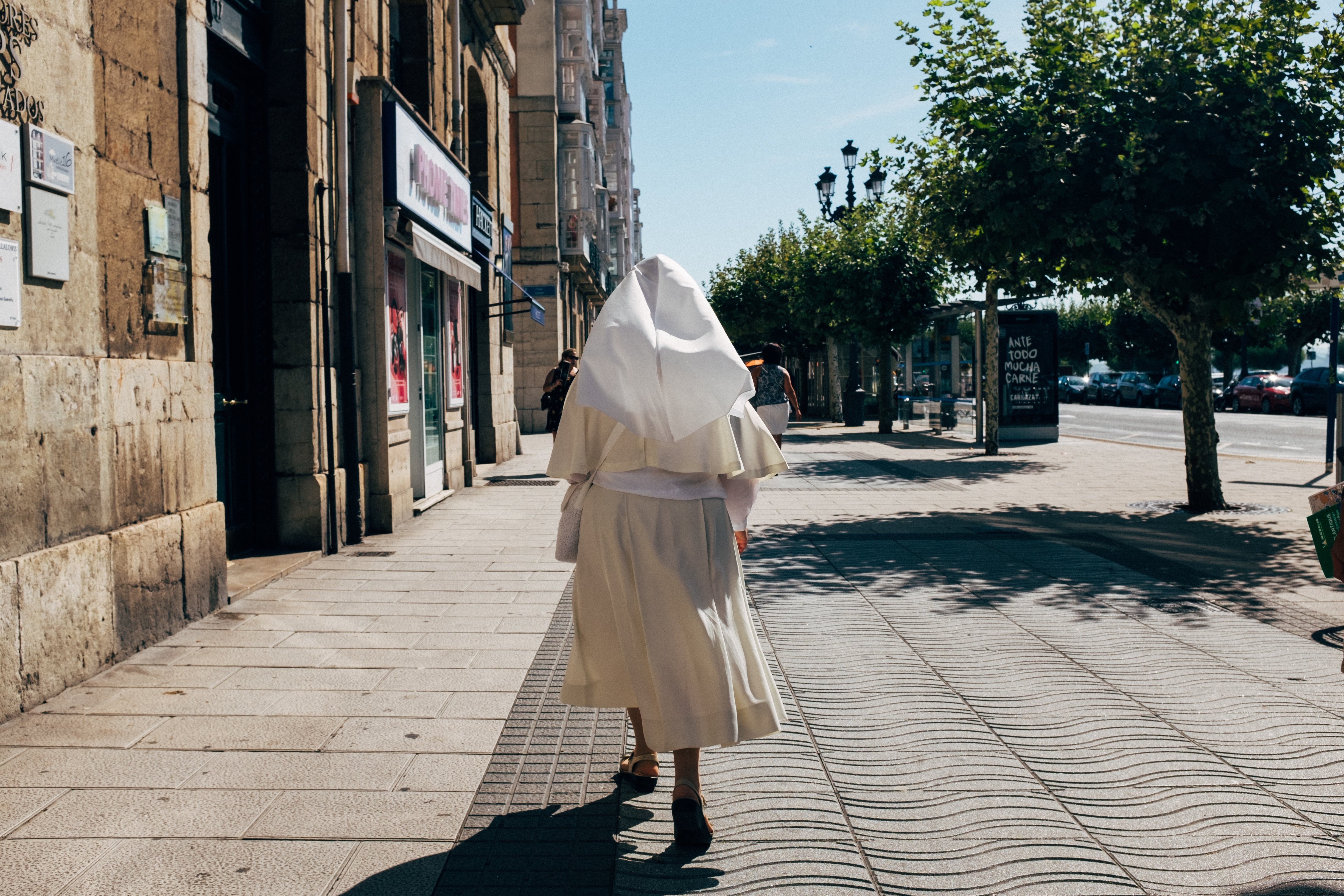 Une religieuse en habit blanc se promène sur un sentier piétonnier ensoleillé