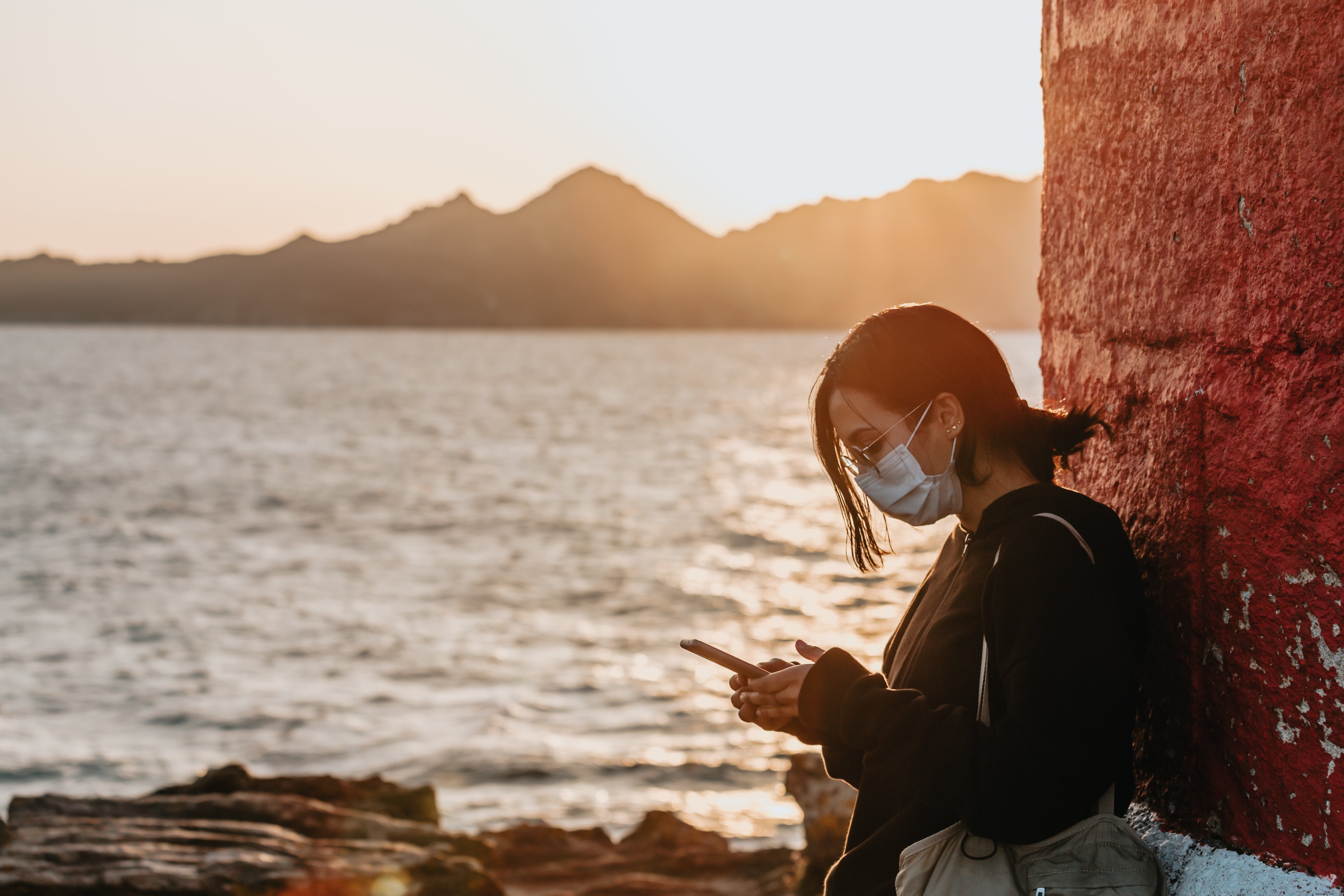 Femme masquée, téléphone à la main, près d’un plan d’eau