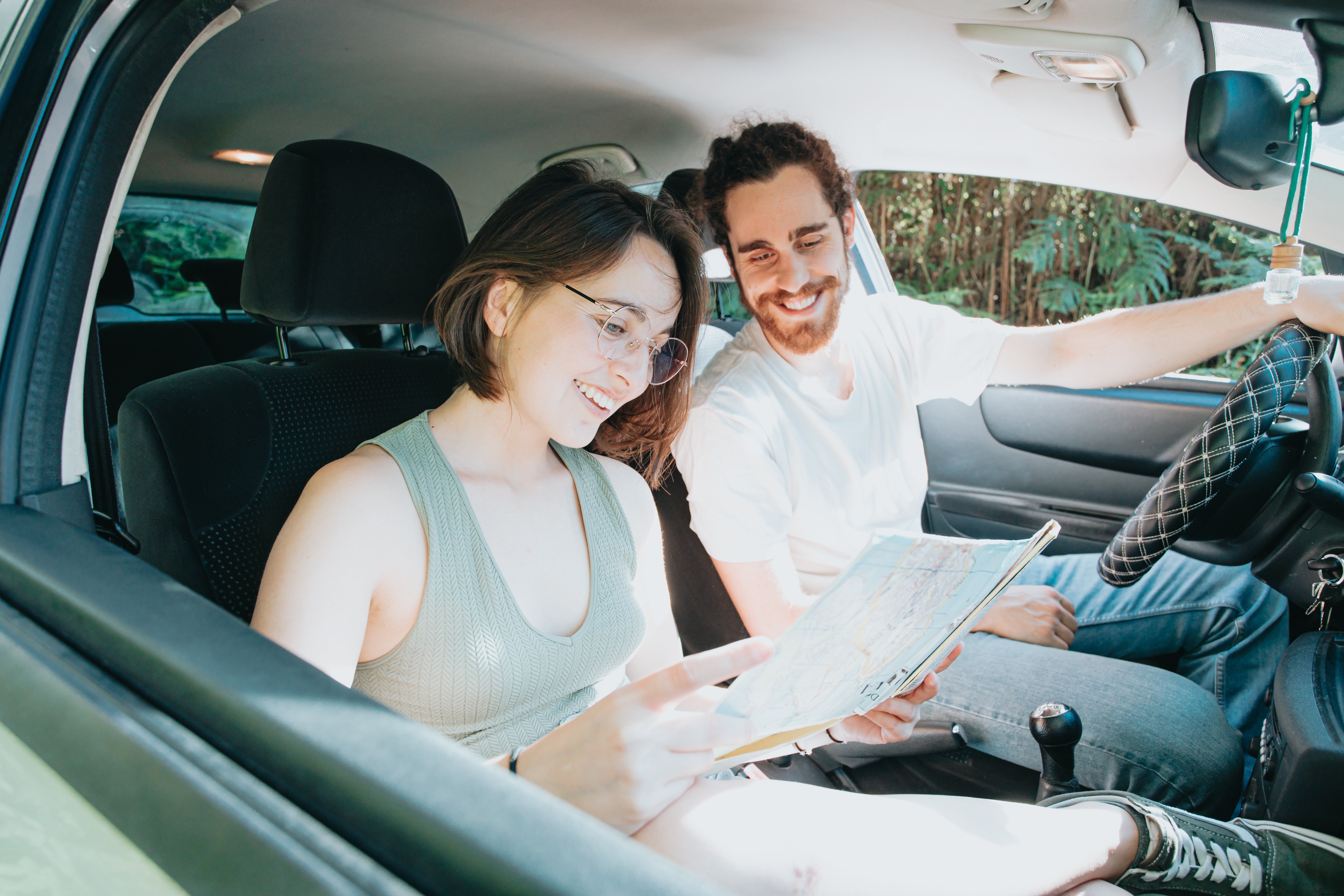 Deux voyageurs en voiture consultent une carte en souriant