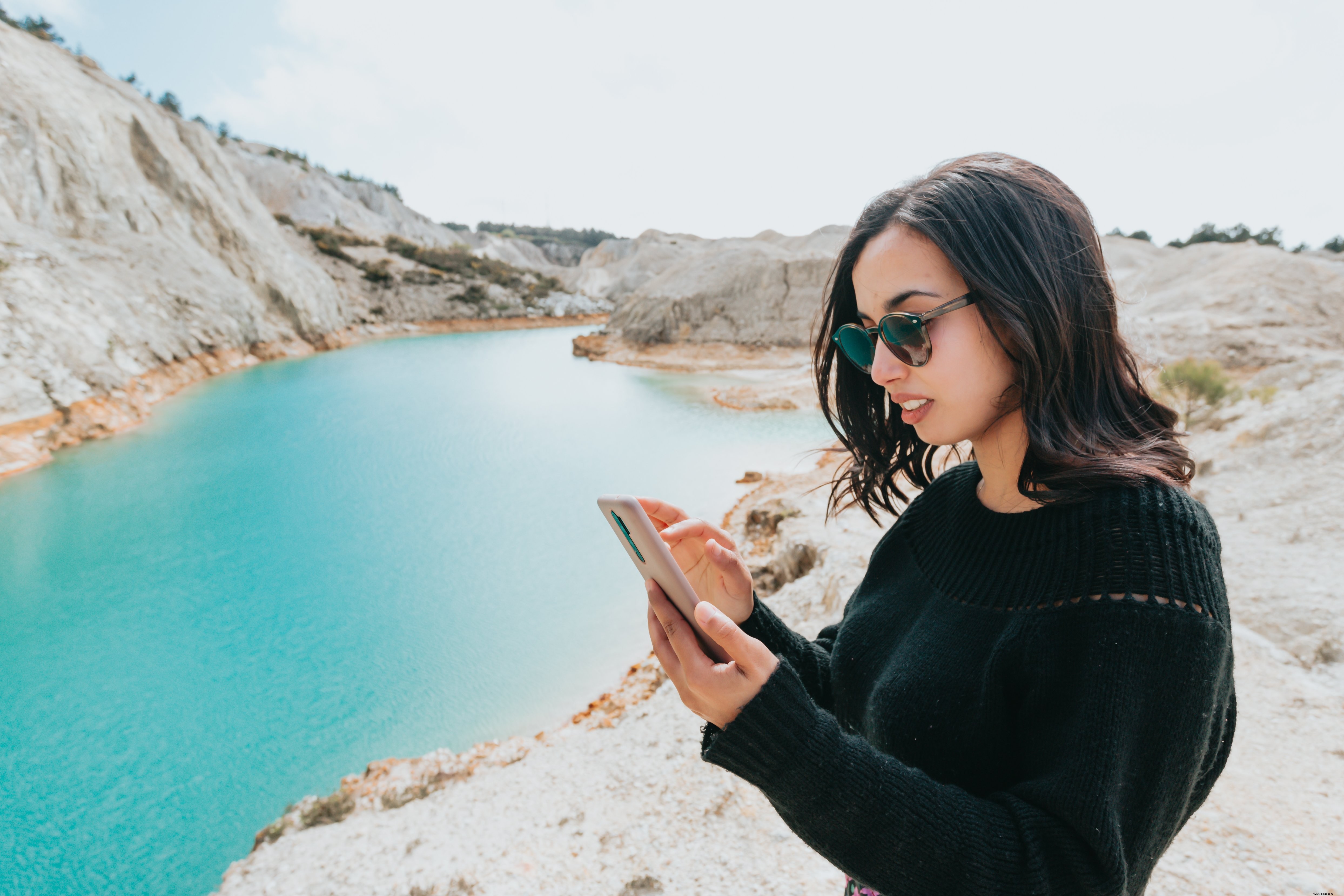 Une femme consulte son smartphone au bord d une eau cristalline