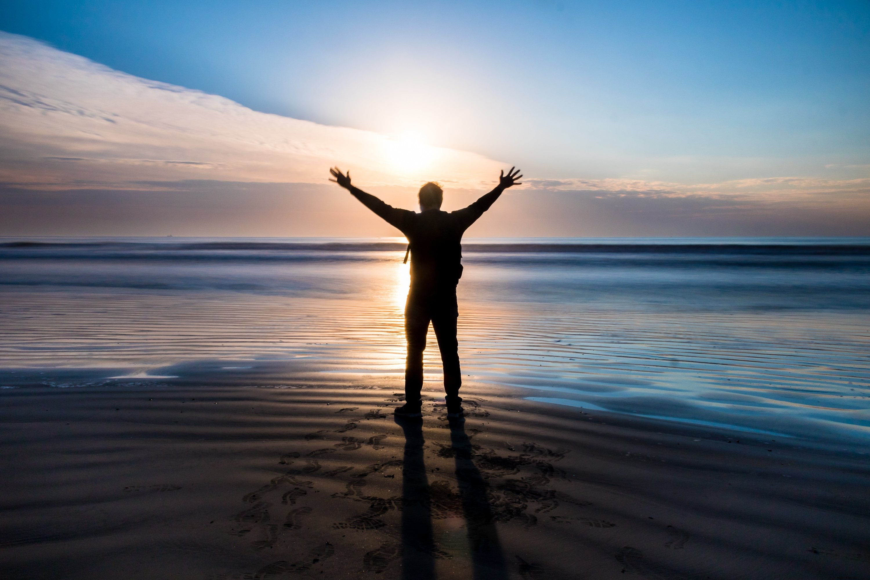 Silhouette d une personne debout sur la plage, les bras levés, au coucher du soleil