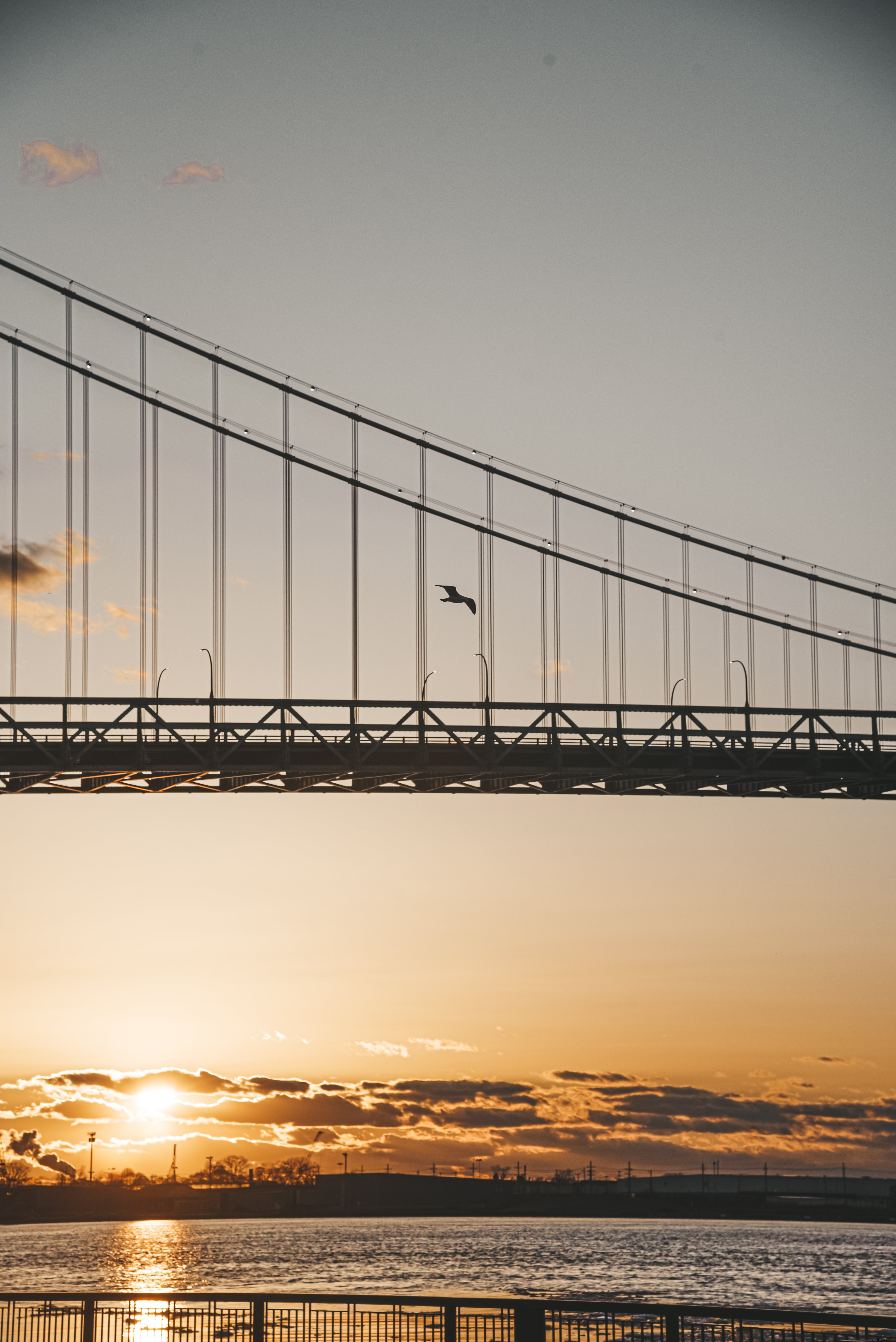 Ciel orange‑jaune au coucher du soleil, reflet sur l’eau et pont partiellement visible